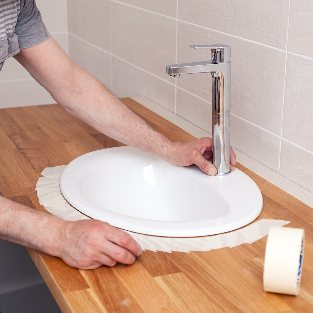 Closeup hand of woodworker with professional cutting tool fretsaw or jigsaw, cut wooden tabletop, sawing plank, brown filings, sawdust. Concept cut a hole for the sink in the bathroom