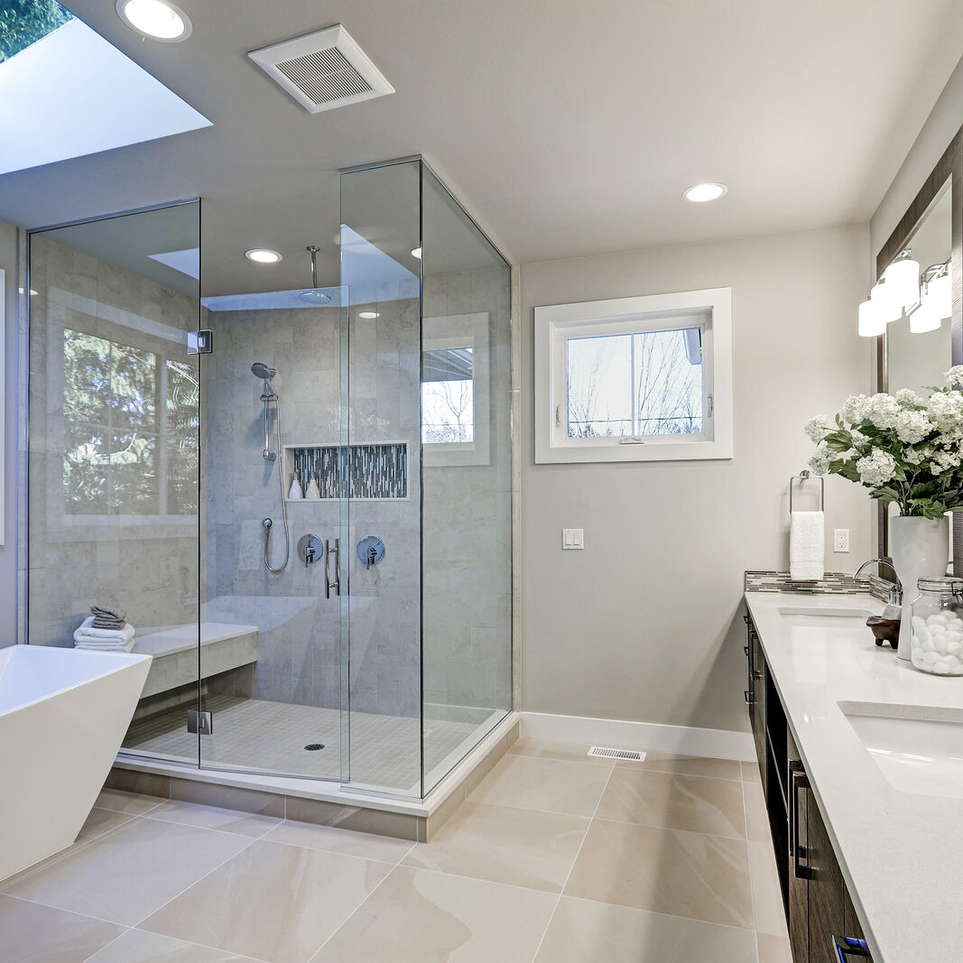 Spacious bathroom in gray tones with heated floors freestanding tub walk-in shower double sink vanity and skylights. Northwest USA