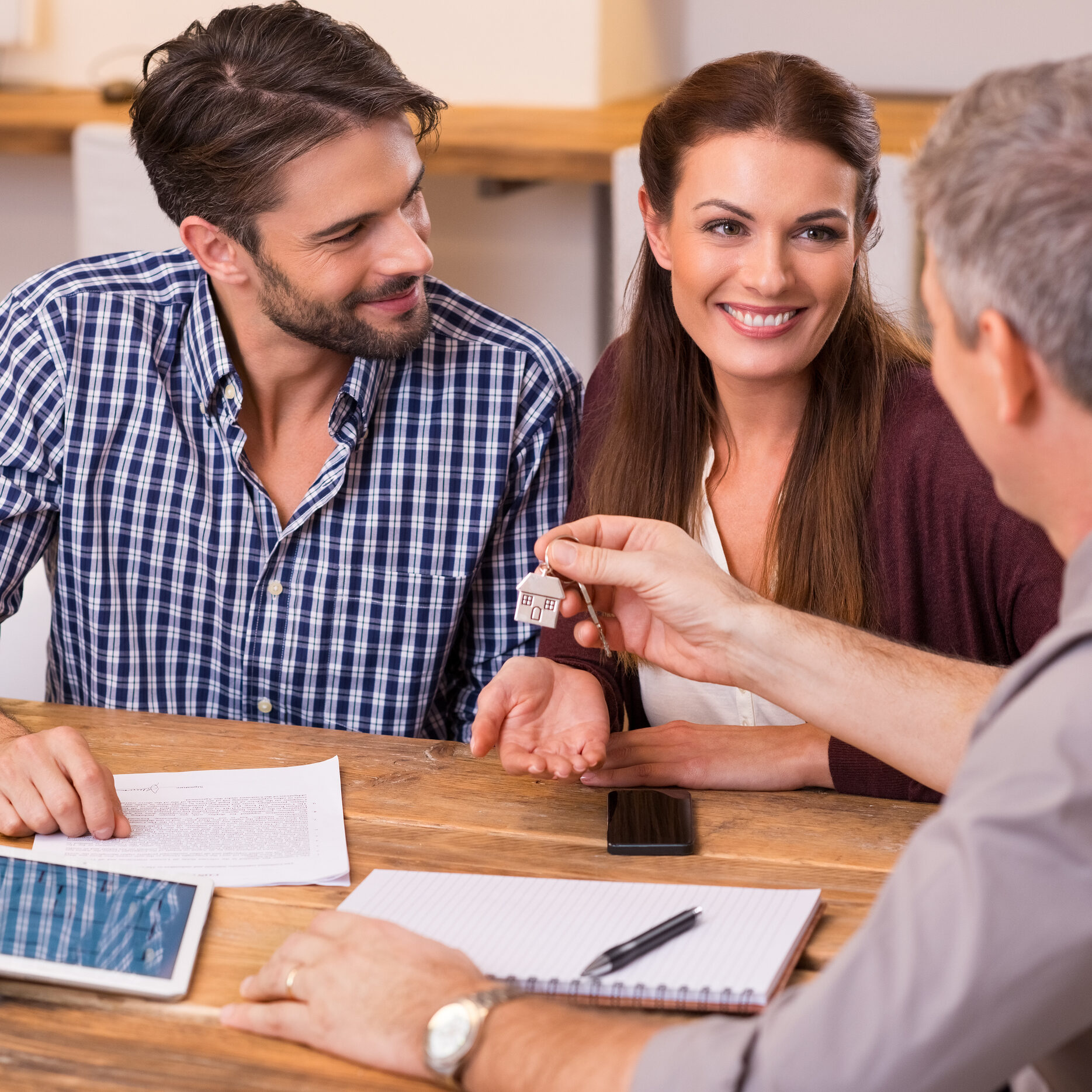 Young happy couple receiving house keys from real estate agent. Giving keys of new house to young couple. Smiling couple signing financial contract for mortgage.